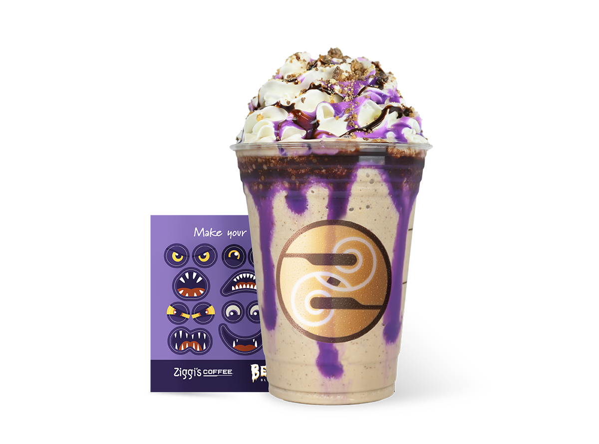 Delectable Ziggi's Coffee drink showcasing layers of rich chocolate and caramel, accented with crushed Twix candy, highlighted by vibrant streaks of purple white chocolate drizzle and decadent dark chocolate drizzle. To the left, playful monster face stickers invite customization with the caption 'Make your own'. The brand's distinct swirl logo prominently displayed on the drink cup.