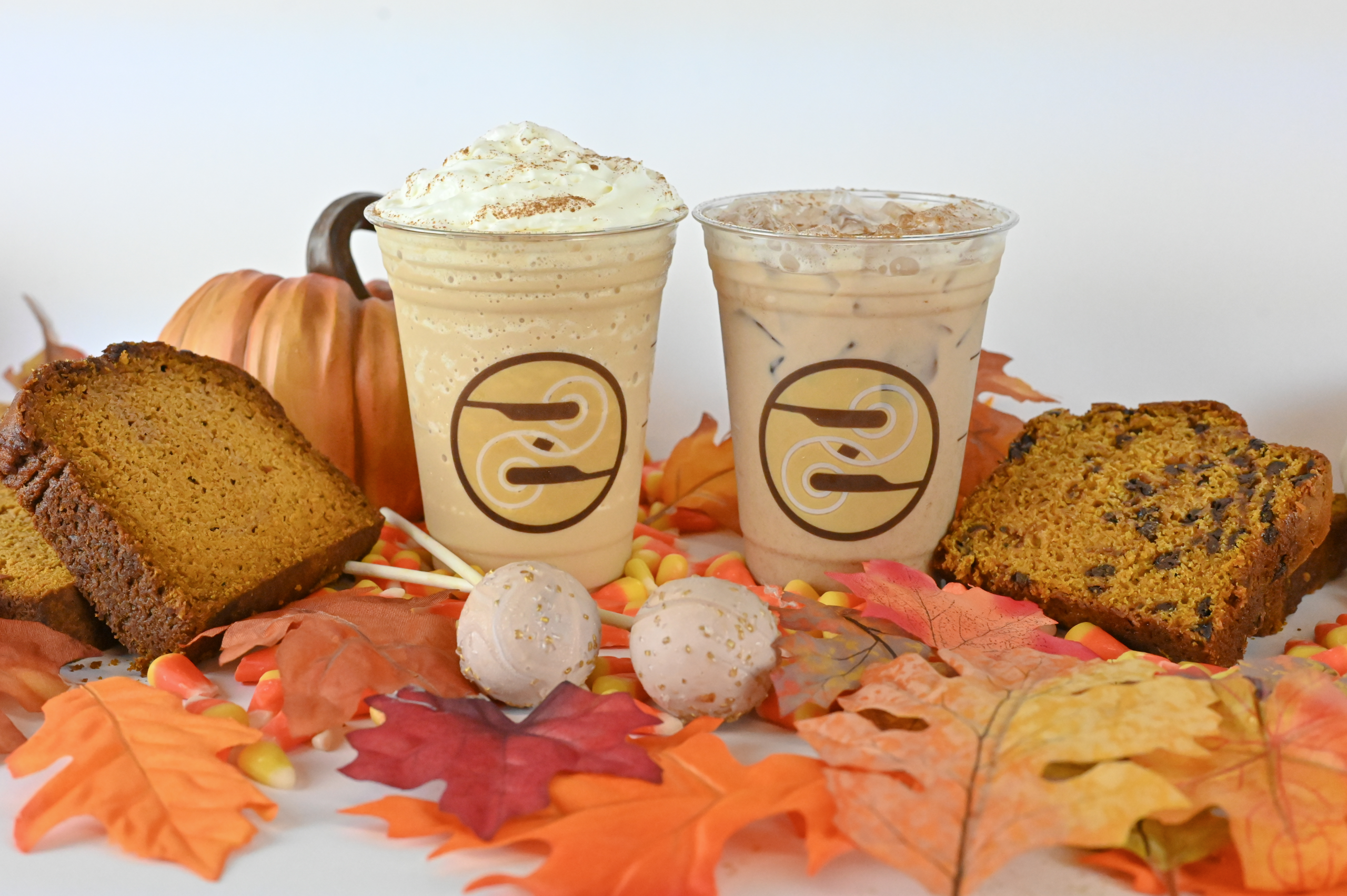 drinks, bread slices and cake pops laying on a pile of leaves with a pumpkin in the background